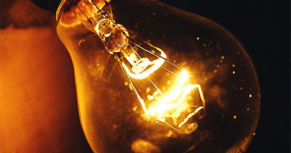 A single glowing incandescent light bulb against a dark background